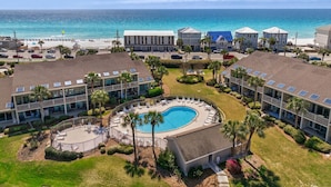 A resort with a central swimming pool, multiple buildings, and a beach view.