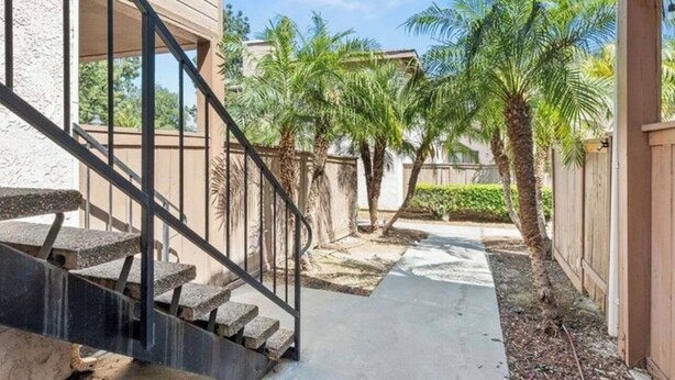 A residential property with a concrete pathway, palm trees, and a wooden fence. - Spacious and Comfy 2-bedroom condo with AC near UC Riverside (Riverside)