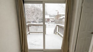 Una stanza con un'ampia porta finestra scorrevole che dà su un balcone, una porta sulla destra e un pavimento piastrellato.