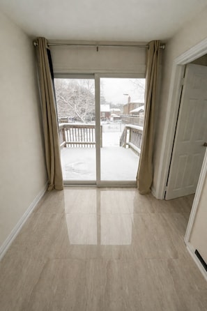 A room with a large sliding glass door leading to a balcony, a door to the right, and a tiled floor.