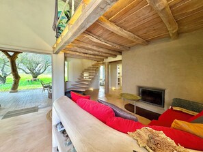Un interior moderno con techo de madera, un sofá con cojines rojos, un televisor y una escalera que lleva a un espacio al aire libre.