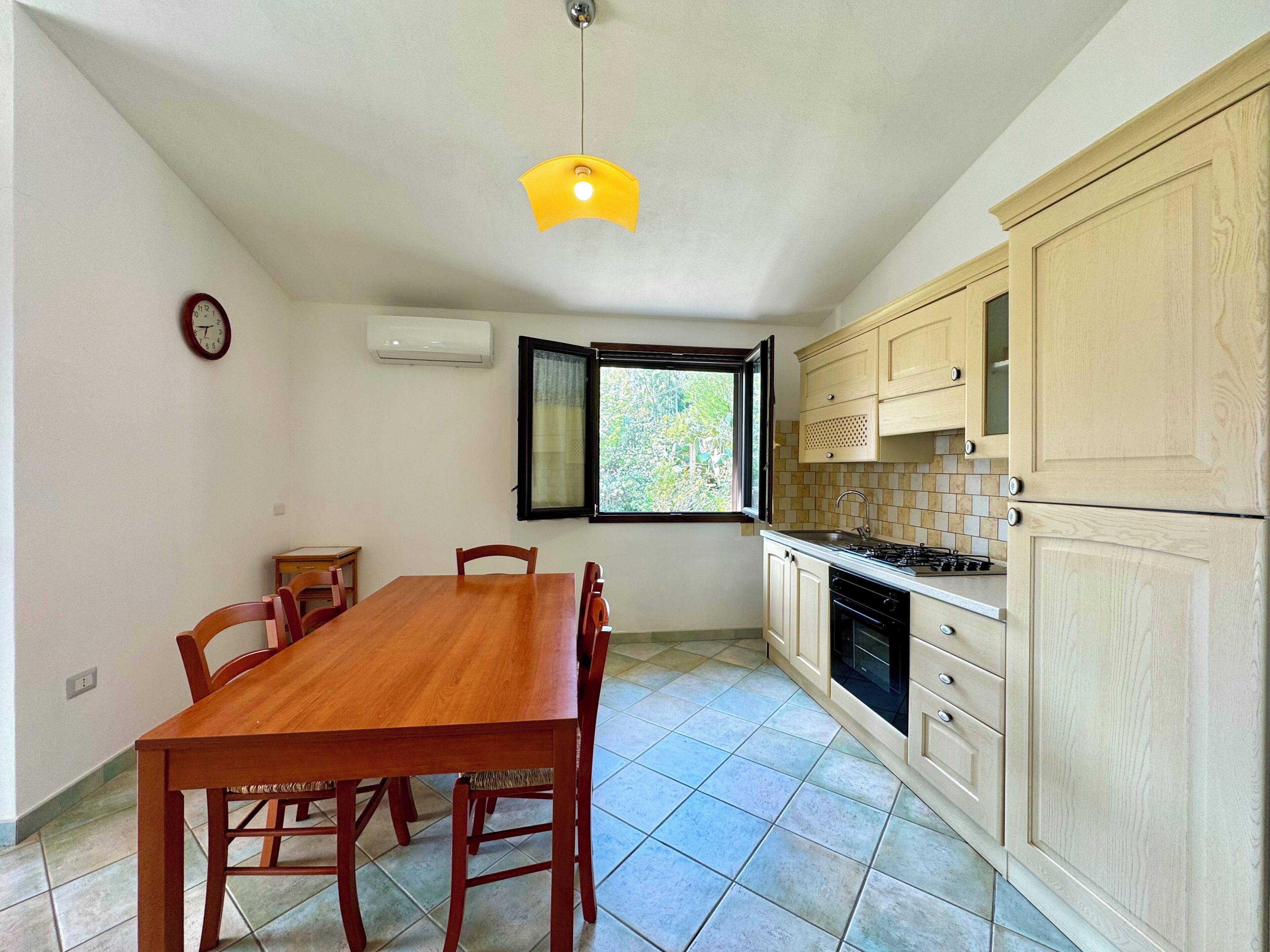 A kitchen with a dining table, chairs, cabinets, a window, and an air conditioning unit.