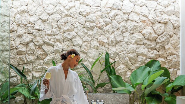 A person in a white bathrobe sitting in a bathtub with a stone wall behind them, surrounded by green plants. - Lomo Boutique Hotel & Villas, Uluwatu (Pecatu)