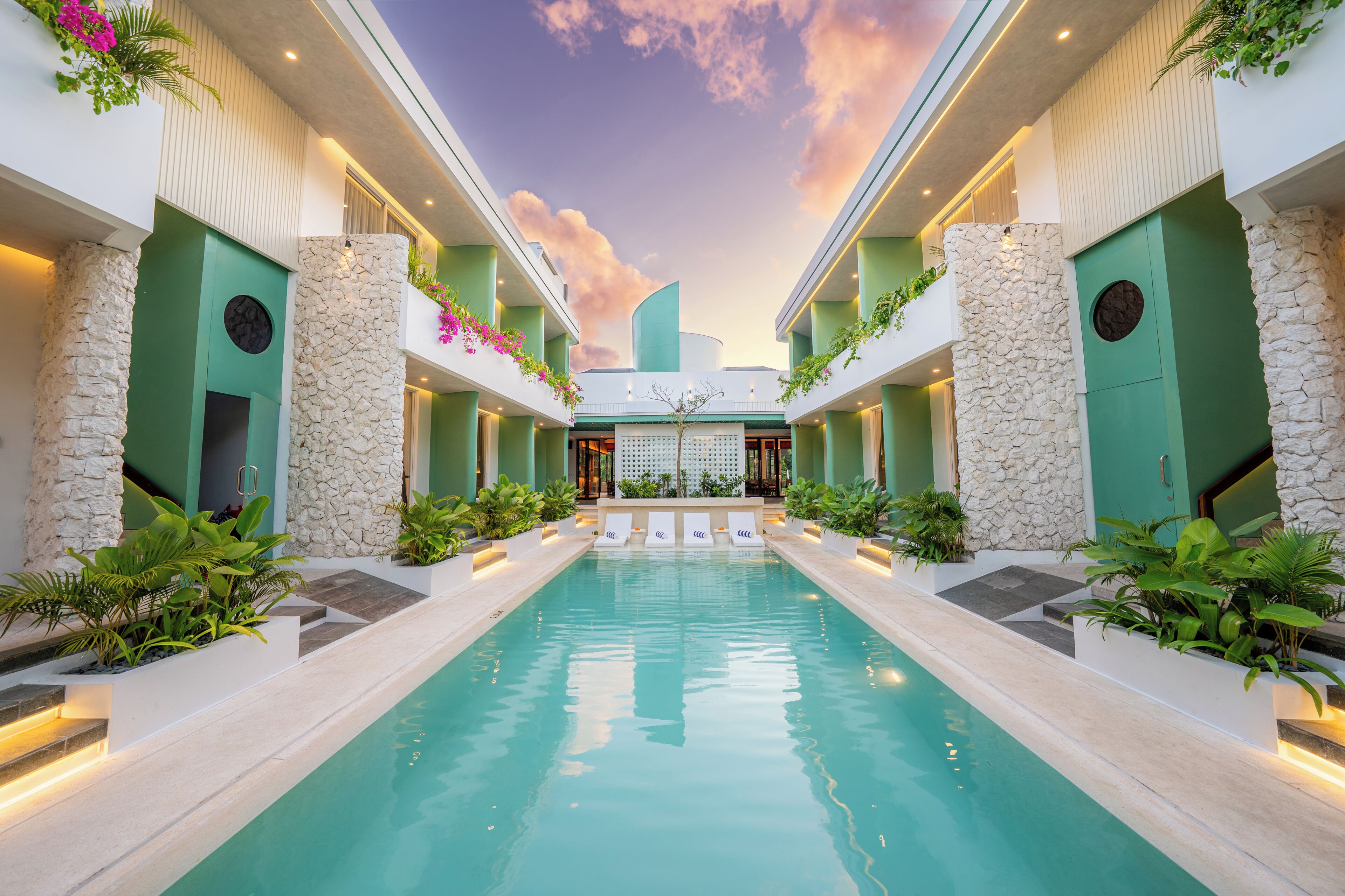 A pool with a stone wall on one side and a balcony with plants on the other.