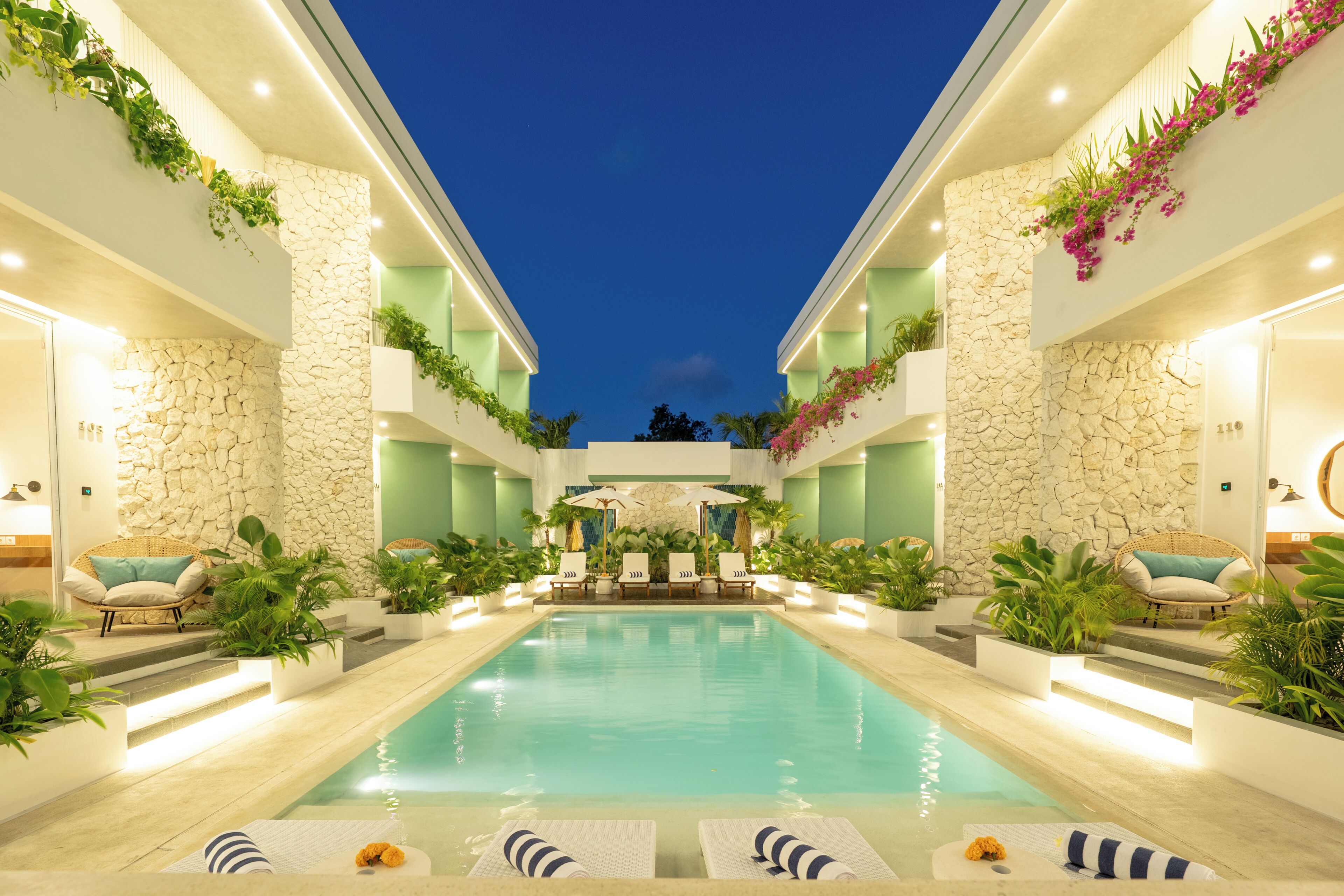 A pool area with lounge chairs, a stone wall, and potted plants.
