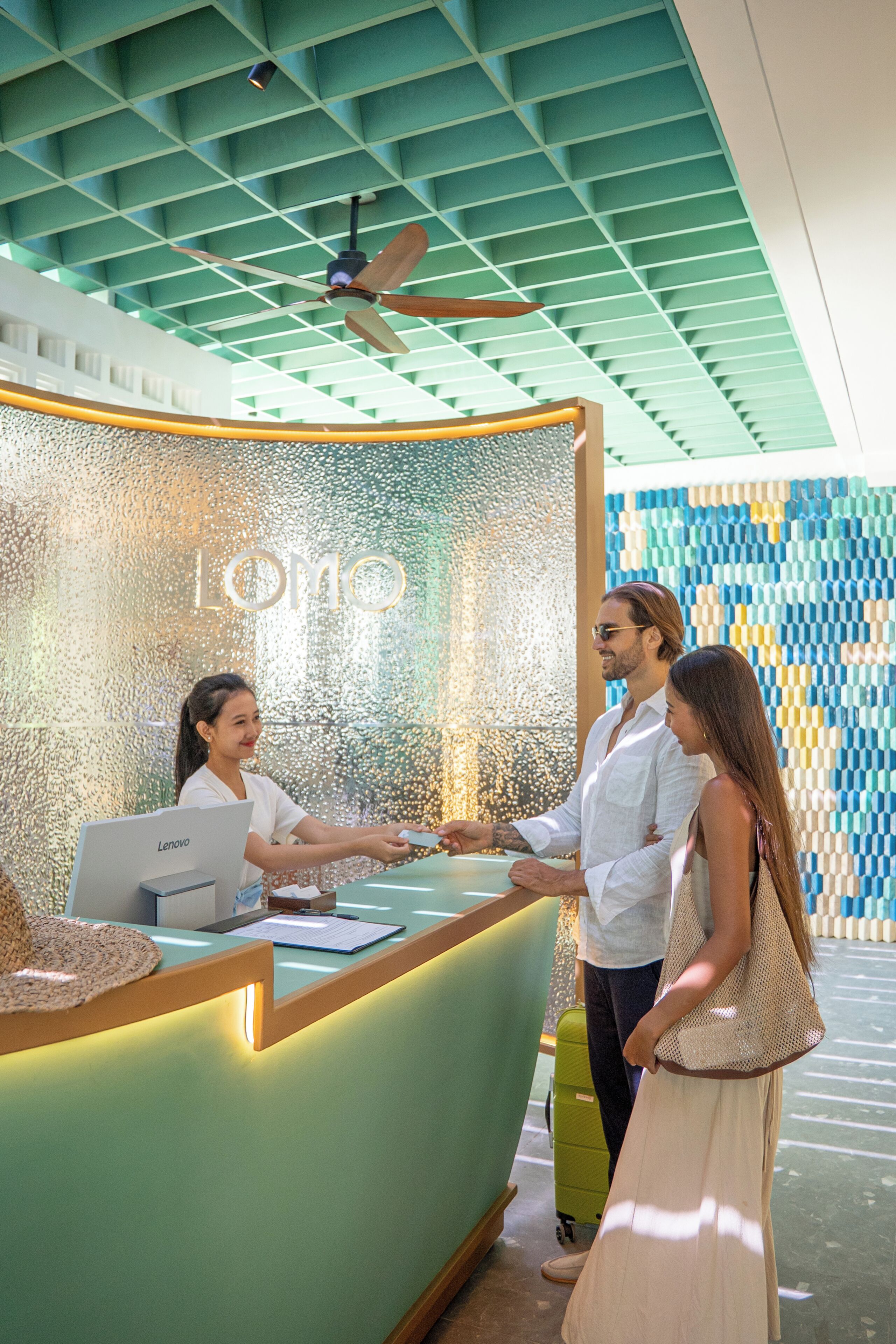 A reception desk with a Lenovo computer, a person standing behind it, and another person in front.