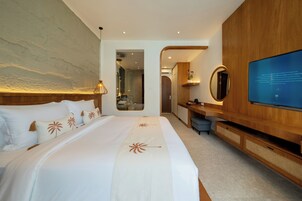 Quarto de hotel moderno com uma cama grande, televisão, secretária de madeira e casa de banho visível através de uma porta aberta.