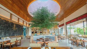 A restaurant with a central seating area, a stone wall, and a large tree in the middle. - Lomo Boutique Hotel & Villas, Uluwatu (Pecatu)