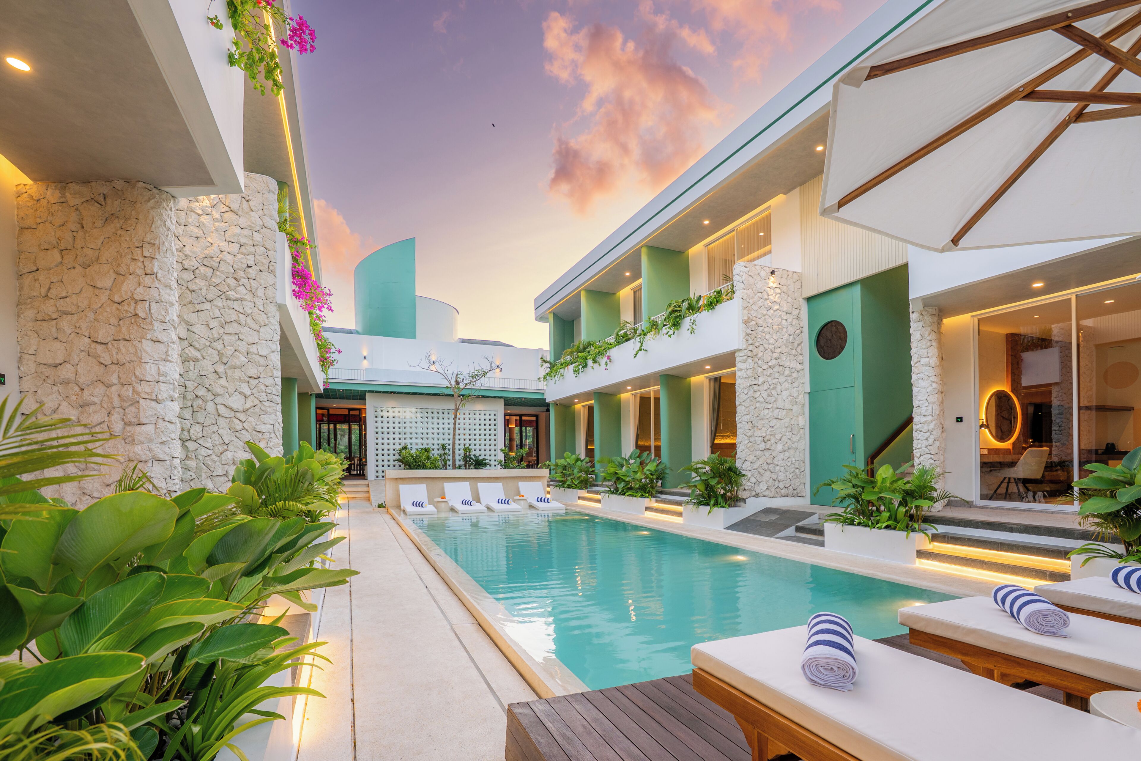 Un área de piscina con sillones de descanso, una pared de piedra y un edificio con fachada verde.