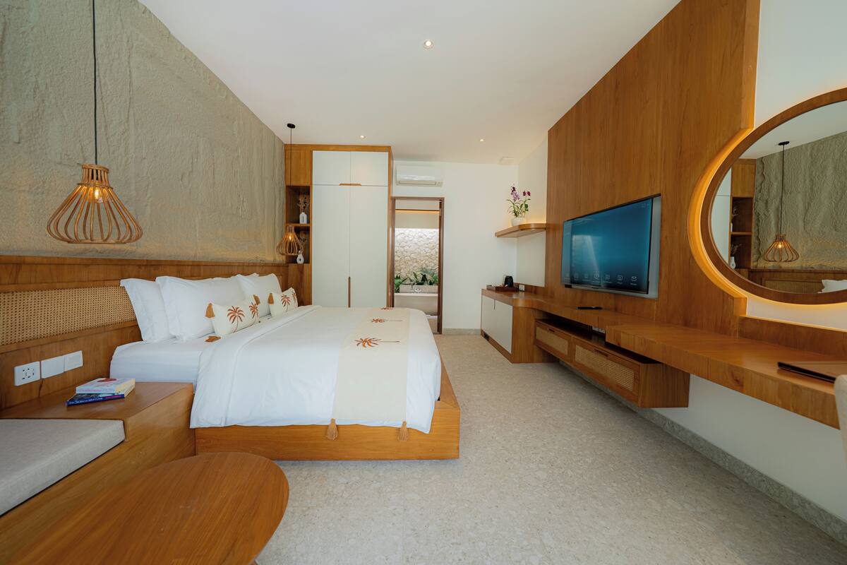 Quarto moderno com uma cama grande, televisão, móveis de madeira e um espelho circular original.
