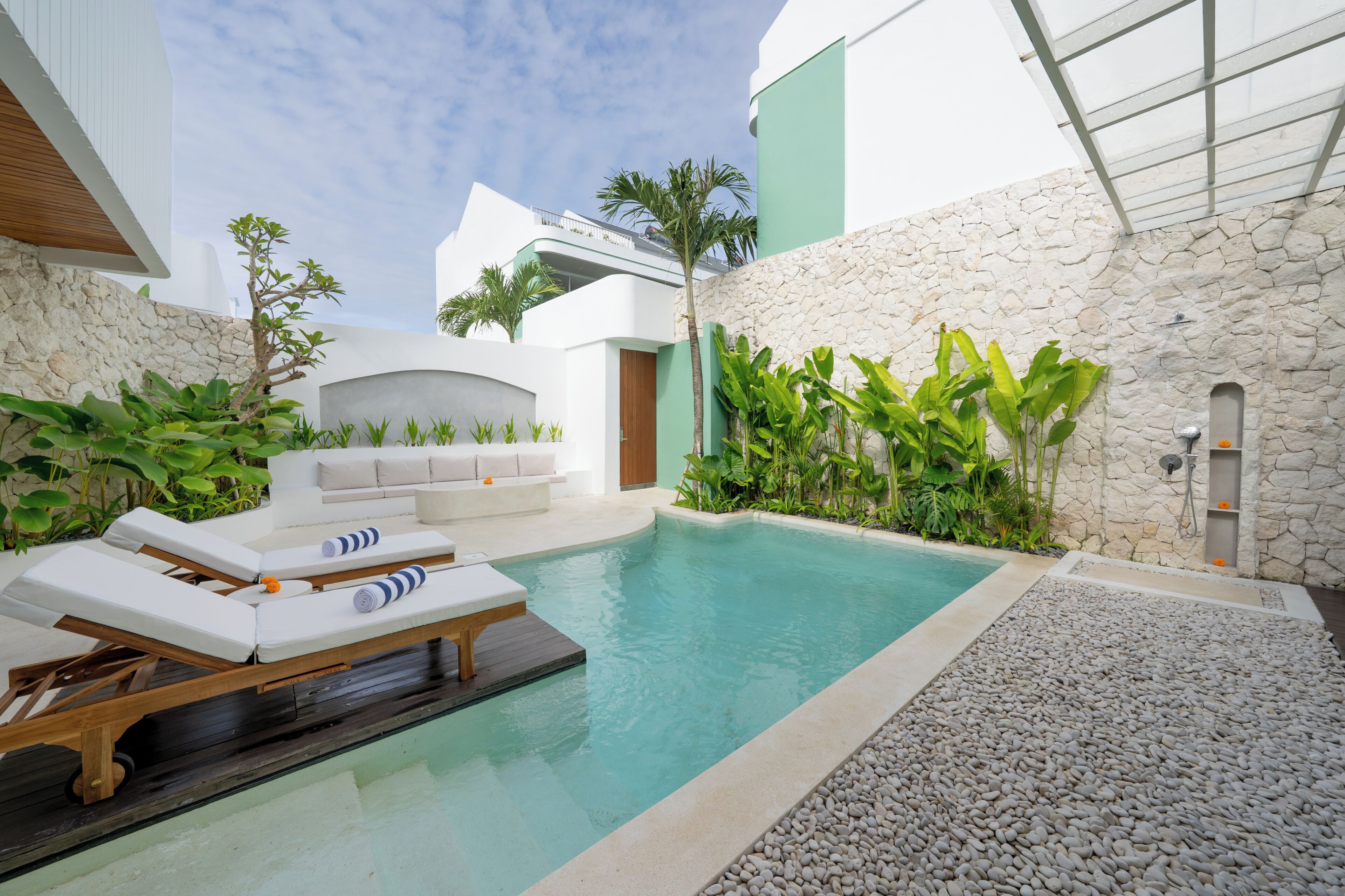 Área de piscina com espreguiçadeiras, parede de pedra e plantas tropicais.