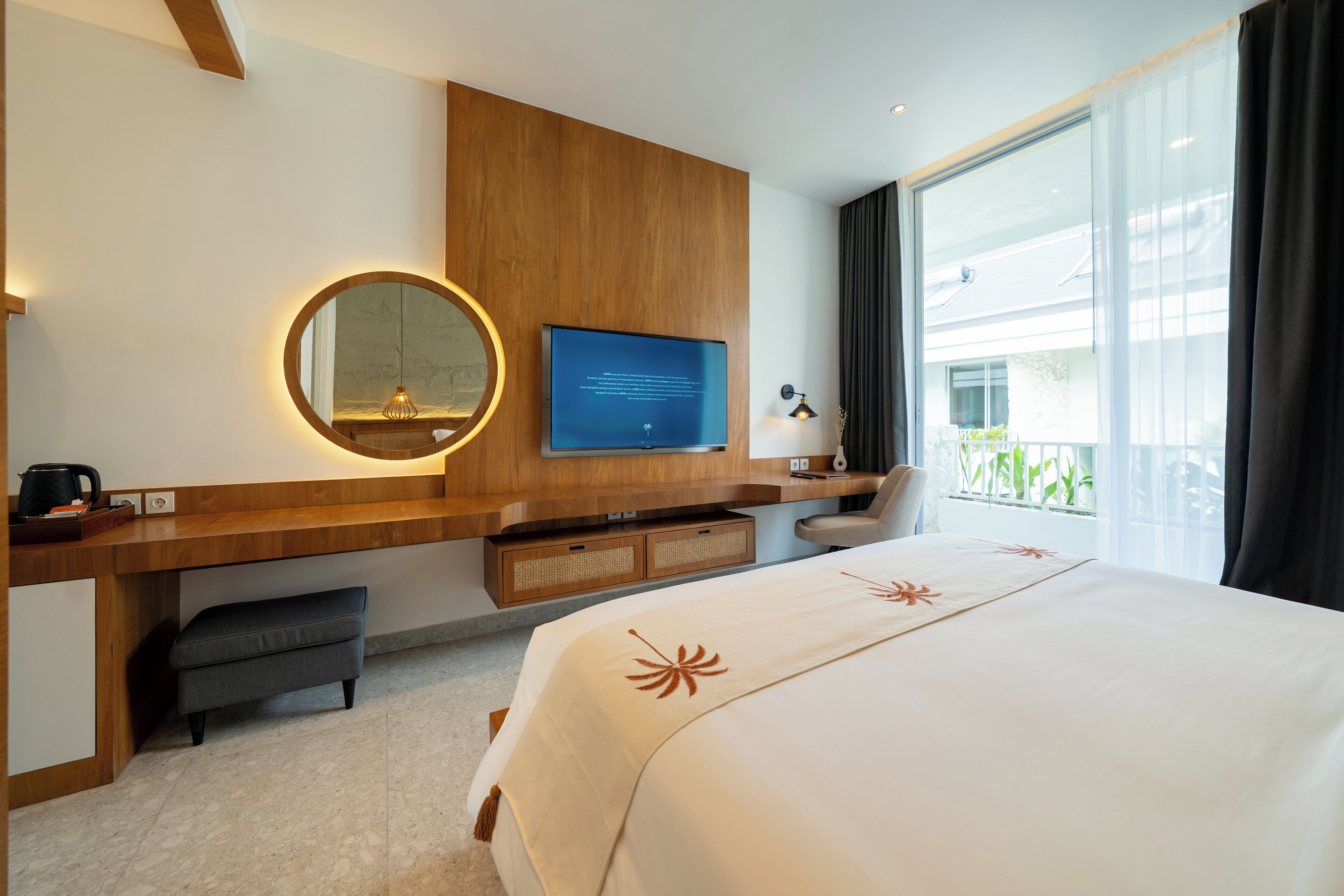 A hotel room with a bed, a TV, a desk with a computer, a chair, and a window with curtains.