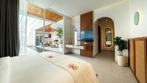 A modern hotel room with a large bed, a TV, a dining area, and a view through a glass door. - Lomo Boutique Hotel & Villas, Uluwatu (Pecatu)