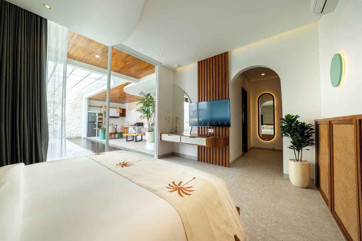 Quarto de hotel moderno com uma cama grande, televisão, área de refeições e vista através de uma porta de vidro.