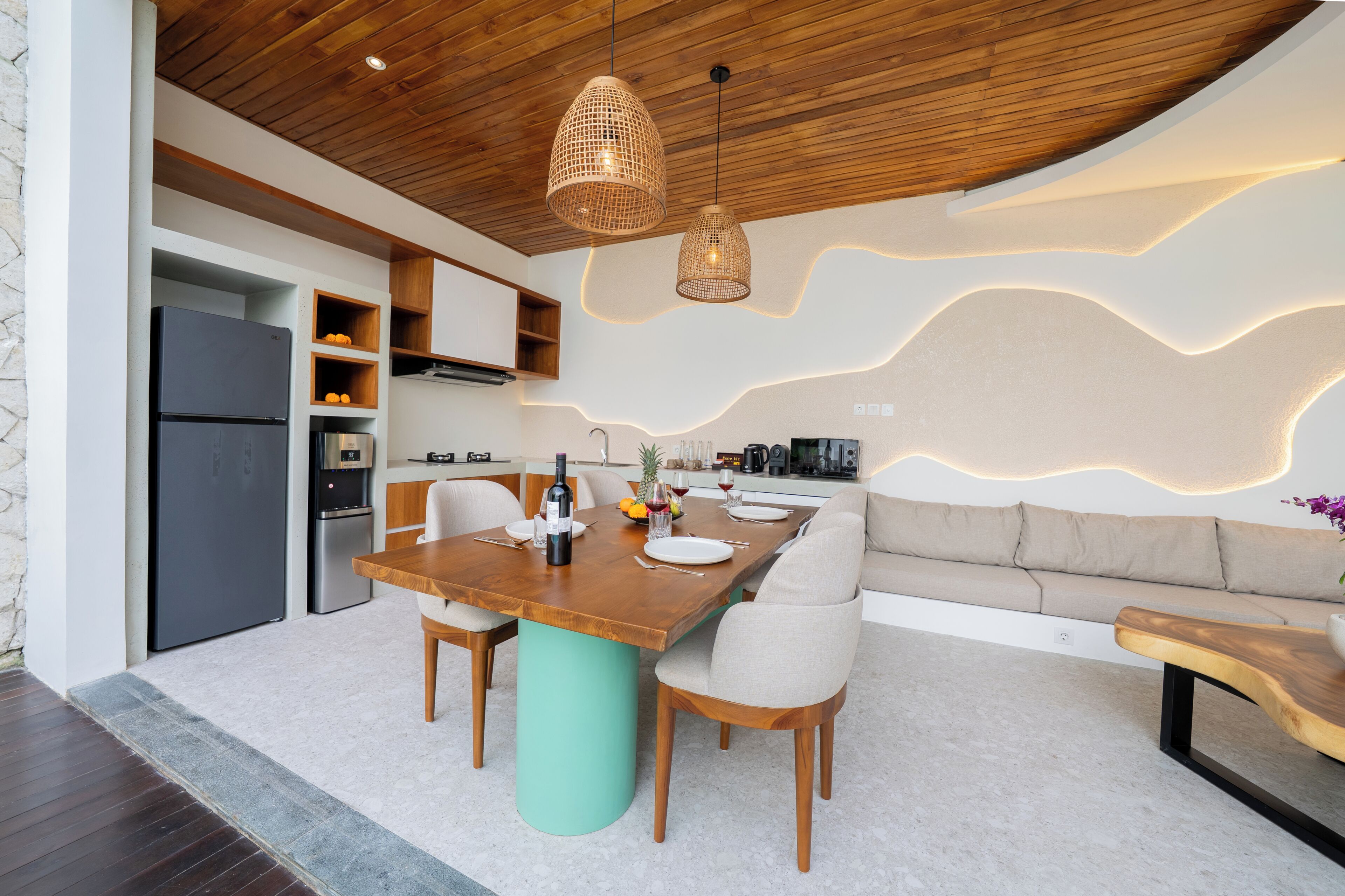 A modern kitchen with a dining area, wooden ceiling, pendant lights, and a built-in oven.
