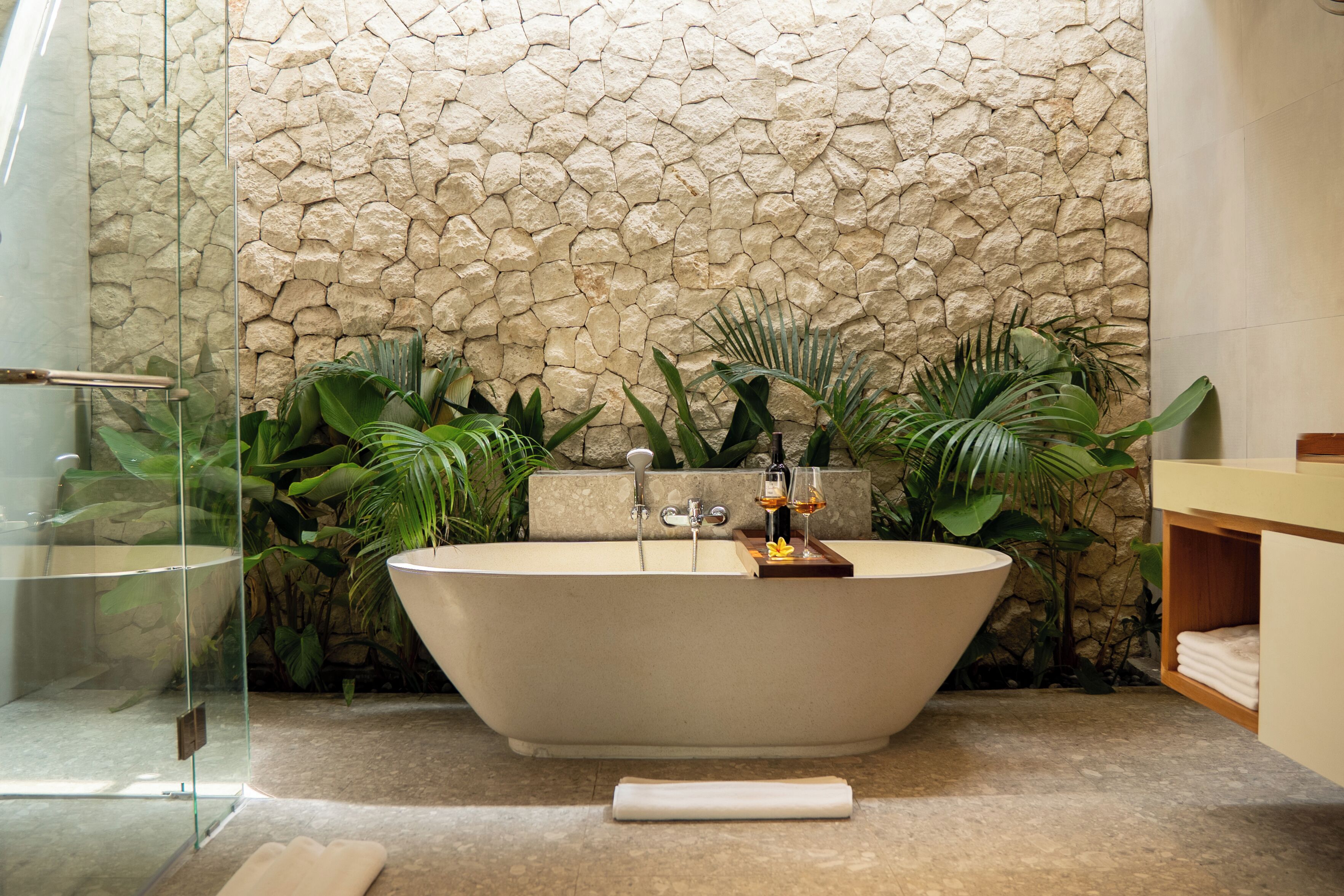 Une salle de bain moderne avec une baignoire sur pieds, une douche à parois de verre et un mur en pierre en arrière-plan.