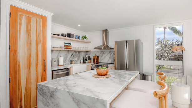 A modern kitchen with a marble island, wooden cabinets, and a large window with a view. - Turtle Bay Renovated Luxury Condo • Walk to Beach • King Bed • AC •  (Kahuku)