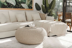 Una sala moderna con un sofá, un reposapiés y una planta grande.