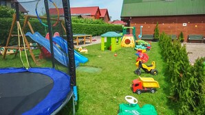Een kinderspeelplaats met een trampoline, een glijbaan en diverse speeltjes.
