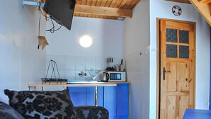 Een compacte keuken met een magnetron, waterkoker en een spoelbak. Een houten deur met ruiten is zichtbaar.