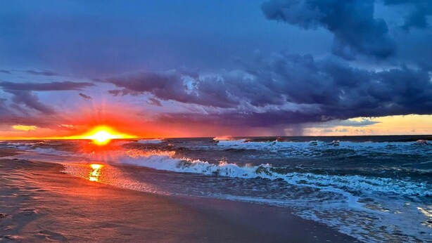 Een zonsondergang boven de oceaan met golven die op het strand breken.