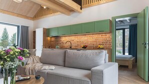 A cozy living area with a sofa, a coffee table, and a view of a kitchen with green cabinets and a brick backsplash. - Stunning home in Dmuchowo with WiFi (Dmuchowo)
