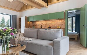 A cozy living area with a sofa, a coffee table, and a view of a kitchen with green cabinets and a brick backsplash. - Stunning home in Dmuchowo with WiFi (Dmuchowo)