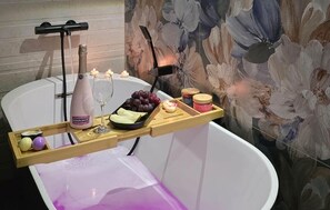 Eine Badewanne mit Tablett, darauf eine Flasche, ein Glas, Trauben, Kerzen und Gläser.