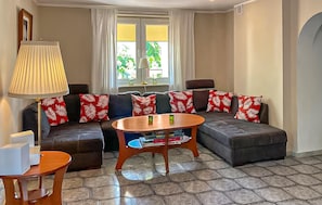 Una sala de estar con sofá modular, una mesa de centro, una lámpara y un ventanal con cortinas.
