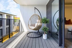 A balcony with a hanging chair, a small potted plant, and a glimpse of a bedroom with a bed and a window. - Central Studio Getaway on Bath Street (Christchurch)