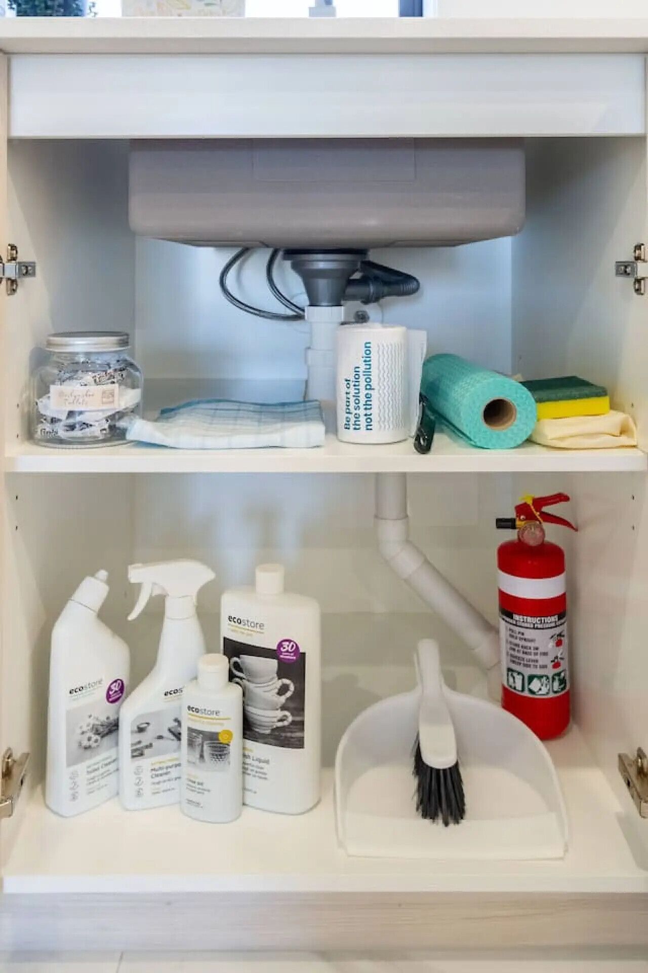 Ein Badezimmerschrank mit Reinigungsmitteln, einem Feuerlöscher und einem Mülleimer.