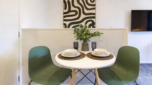Un'area pranzo con un tavolo rotondo, due sedie, un vaso con fiori e un'opera d'arte appesa al muro.
