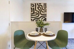 A dining area with a round table, two chairs, a vase with flowers, and a wall-mounted artwork. - Central Studio Getaway on Bath Street (Christchurch)