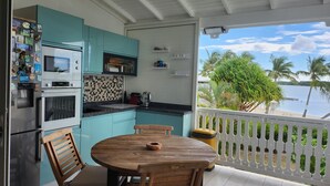 Eine Küche mit türkis-blauen Schränken, einem Holzespeisetisch und Blick auf einen Strand mit Palmen.