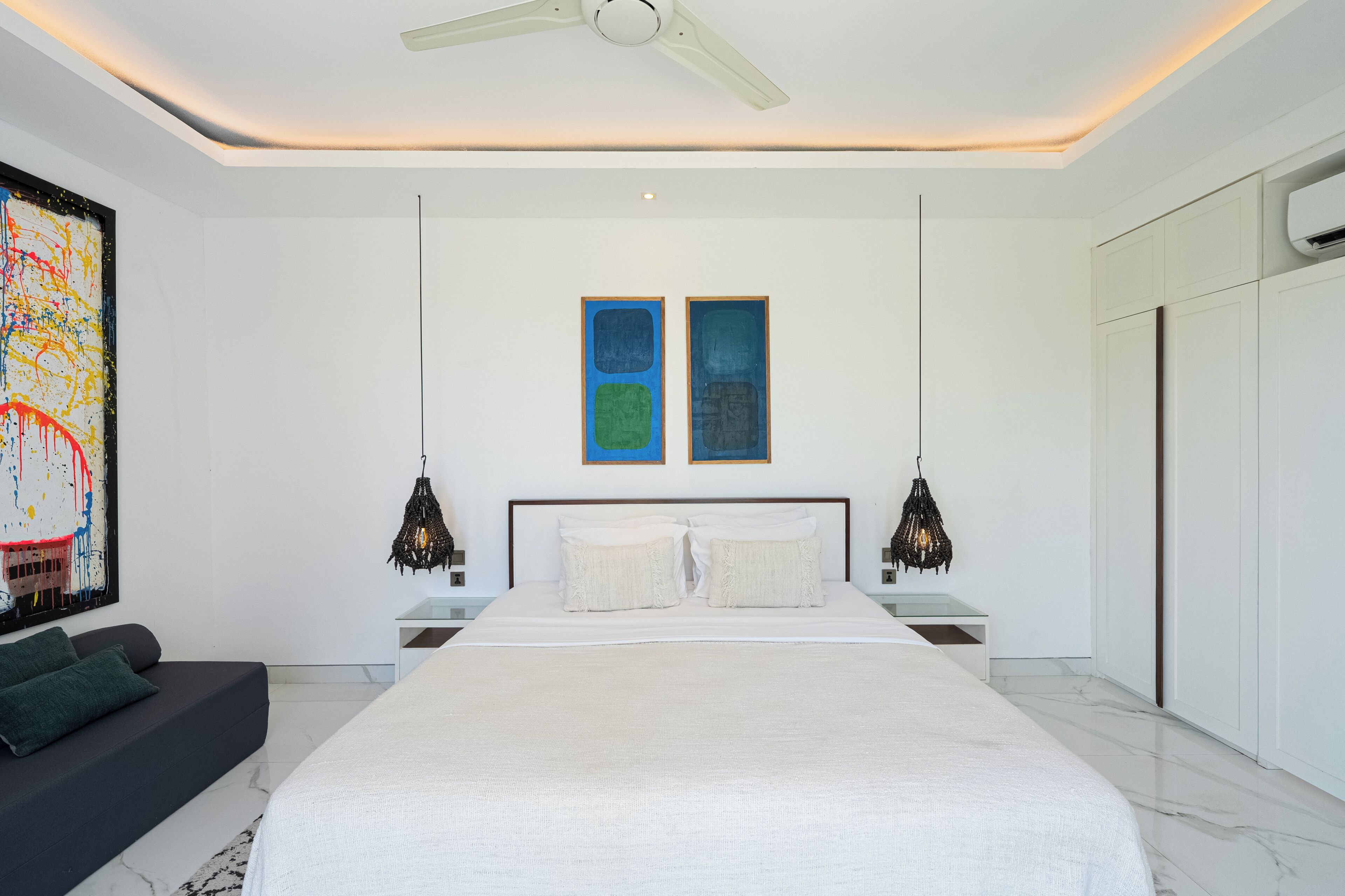A modern bedroom with a large bed, two wall art pieces, a ceiling fan, and a black pendant light.