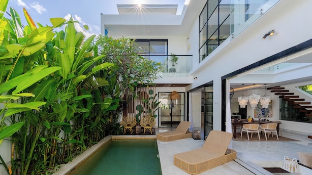 Ein modernes Haus mit Swimmingpool, Sitzgelegenheiten im Freien und einer Glaskonstruktion als Treppe.