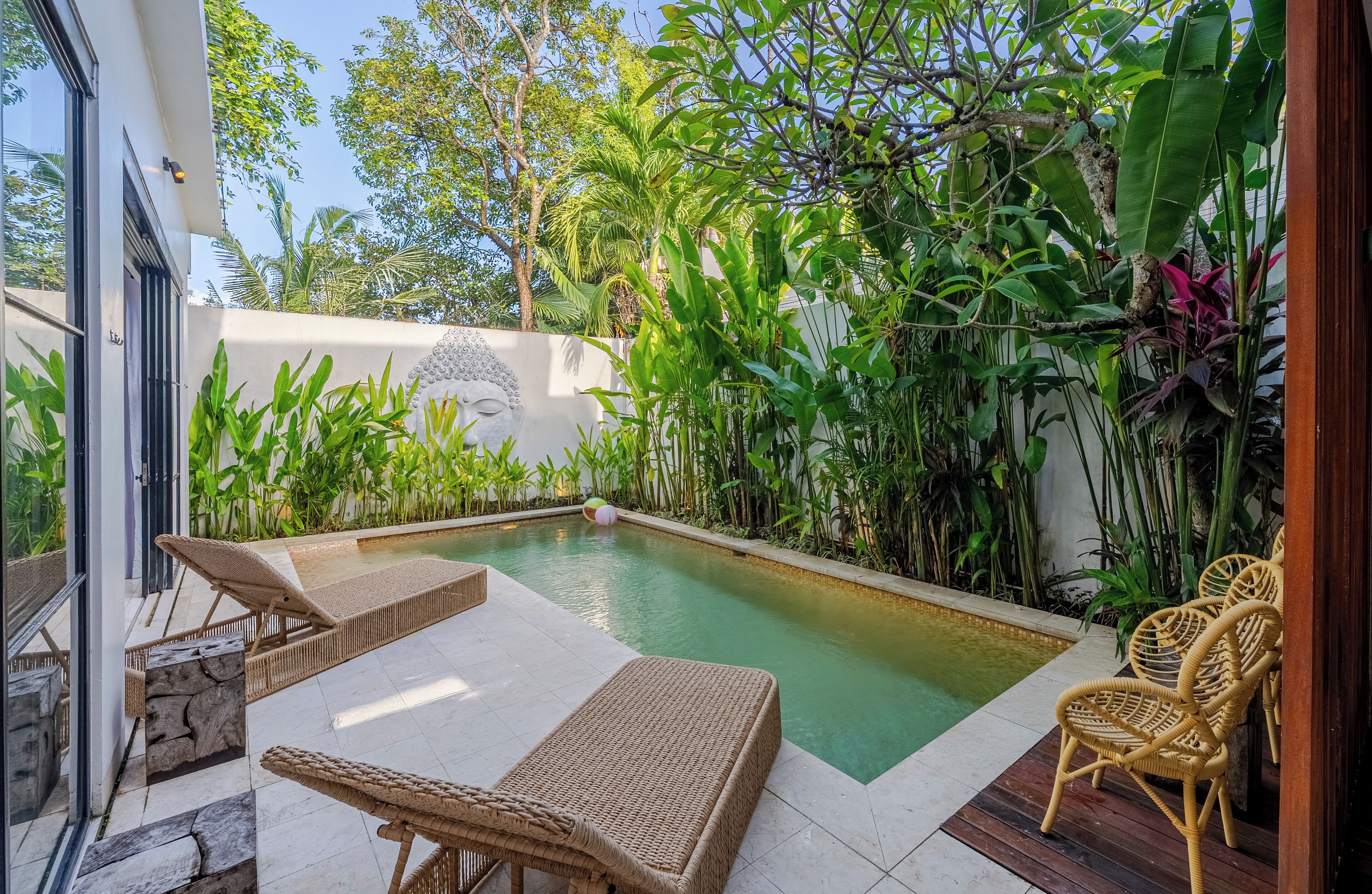 Un área de piscina privada con sillones de descanso, un muro de piedra y exuberante vegetación tropical.