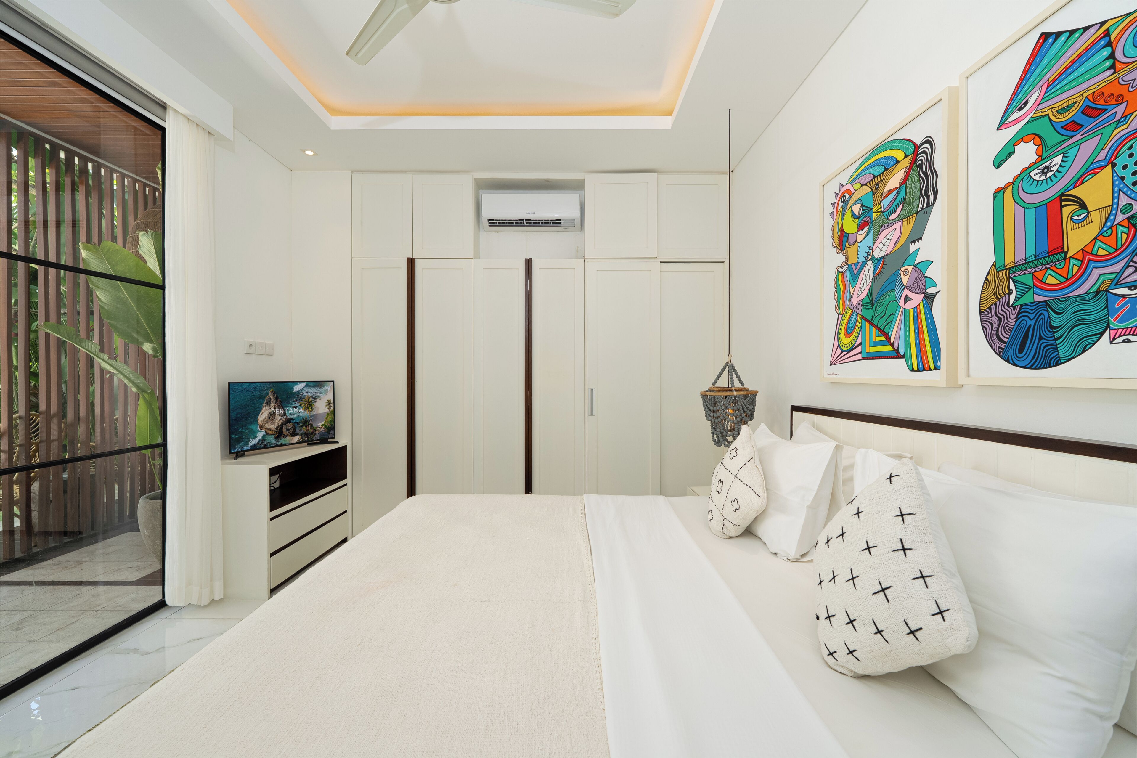 A modern bedroom with a large bed, a TV, a ceiling fan, and artwork on the walls.