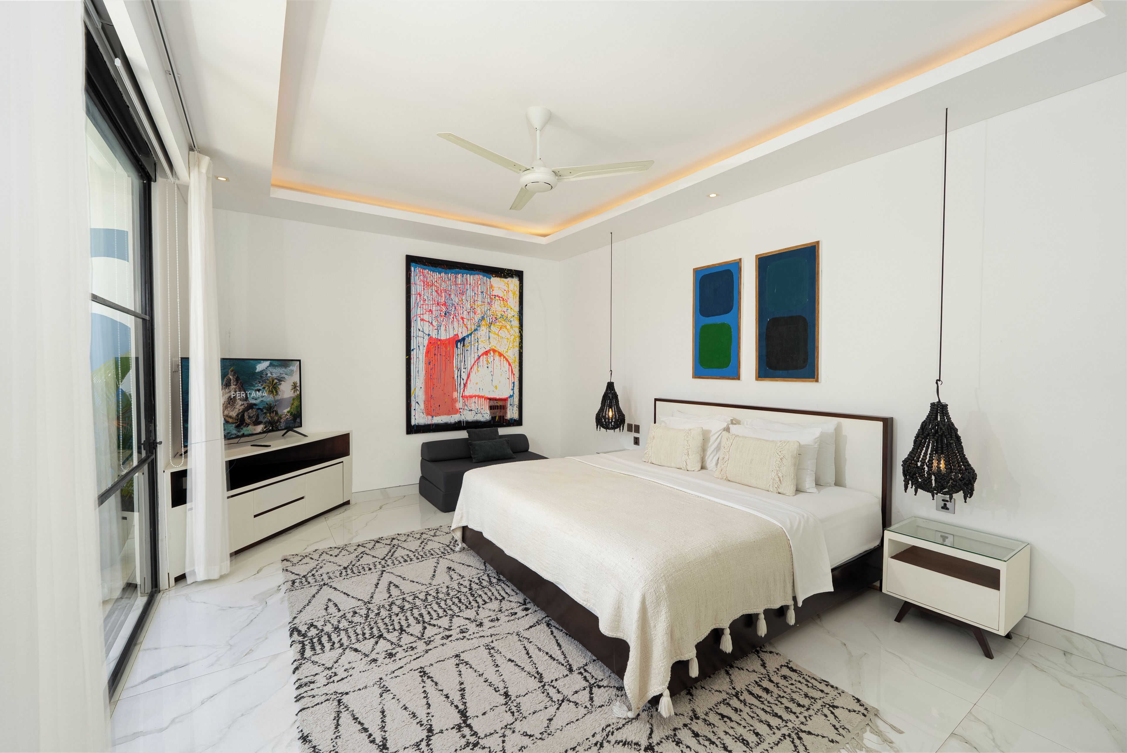 A modern bedroom with a bed, a TV, artwork, and a ceiling fan.