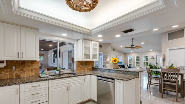 A modern kitchen with white cabinets, granite countertops, and a built-in dishwasher. - Waterfront Oasis - Fish from Backyard, Heated Pool & Spa (Cape Coral)