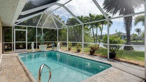 A covered swimming pool with a view of palm trees and a lake. - Waterfront Oasis - Fish from Backyard, Heated Pool & Spa (Cape Coral)