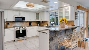 A modern kitchen with white cabinets, a granite countertop, a built-in microwave, and a large island with bar seating. - Waterfront Oasis - Fish from Backyard, Heated Pool & Spa (Cape Coral)