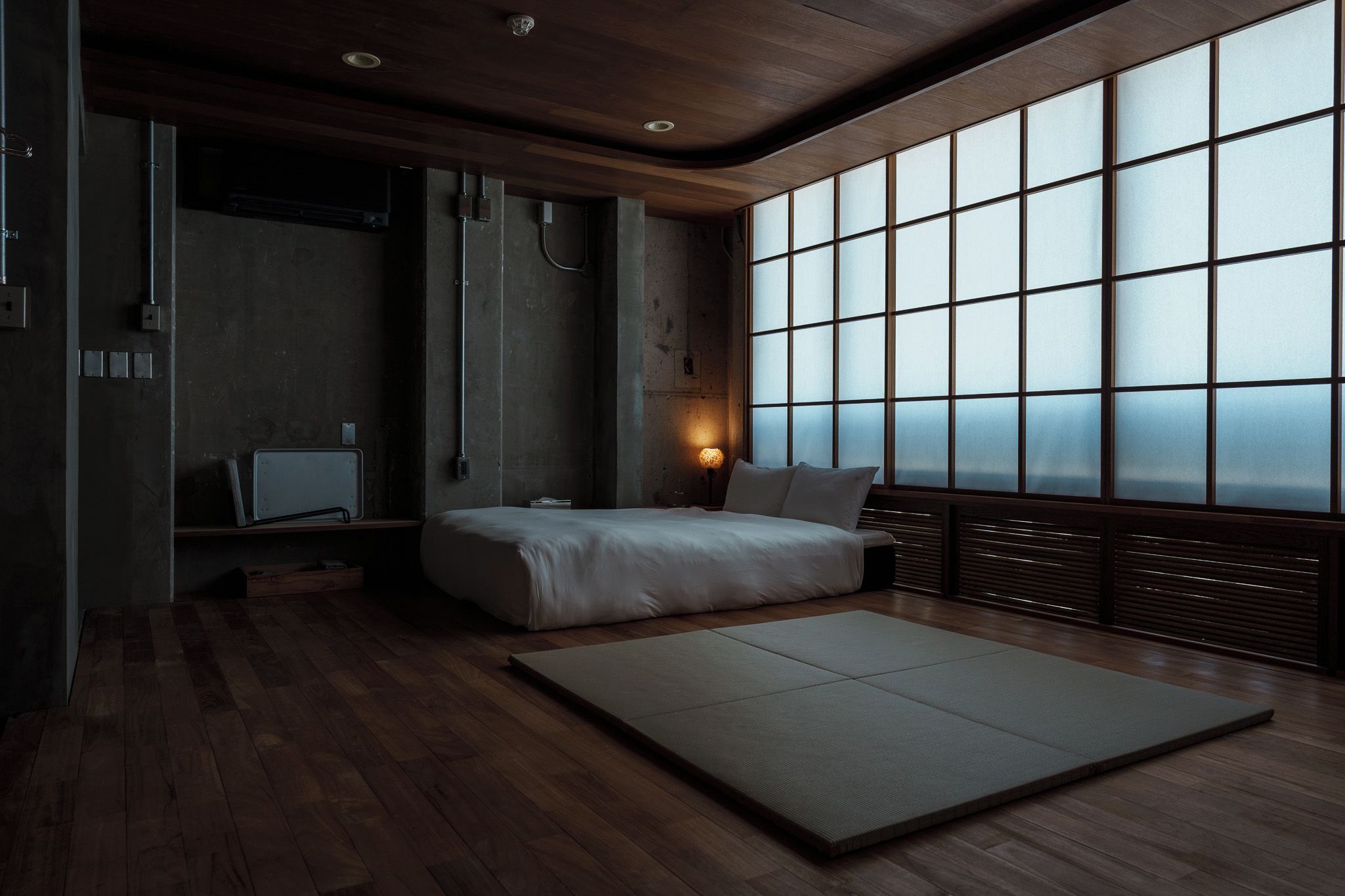 A bedroom with a large window, a bed, a bedside table, and a futon.