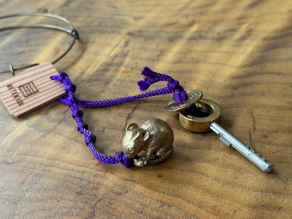 A wooden keychain with a mouse figurine, a small metal container, and a purple cord.