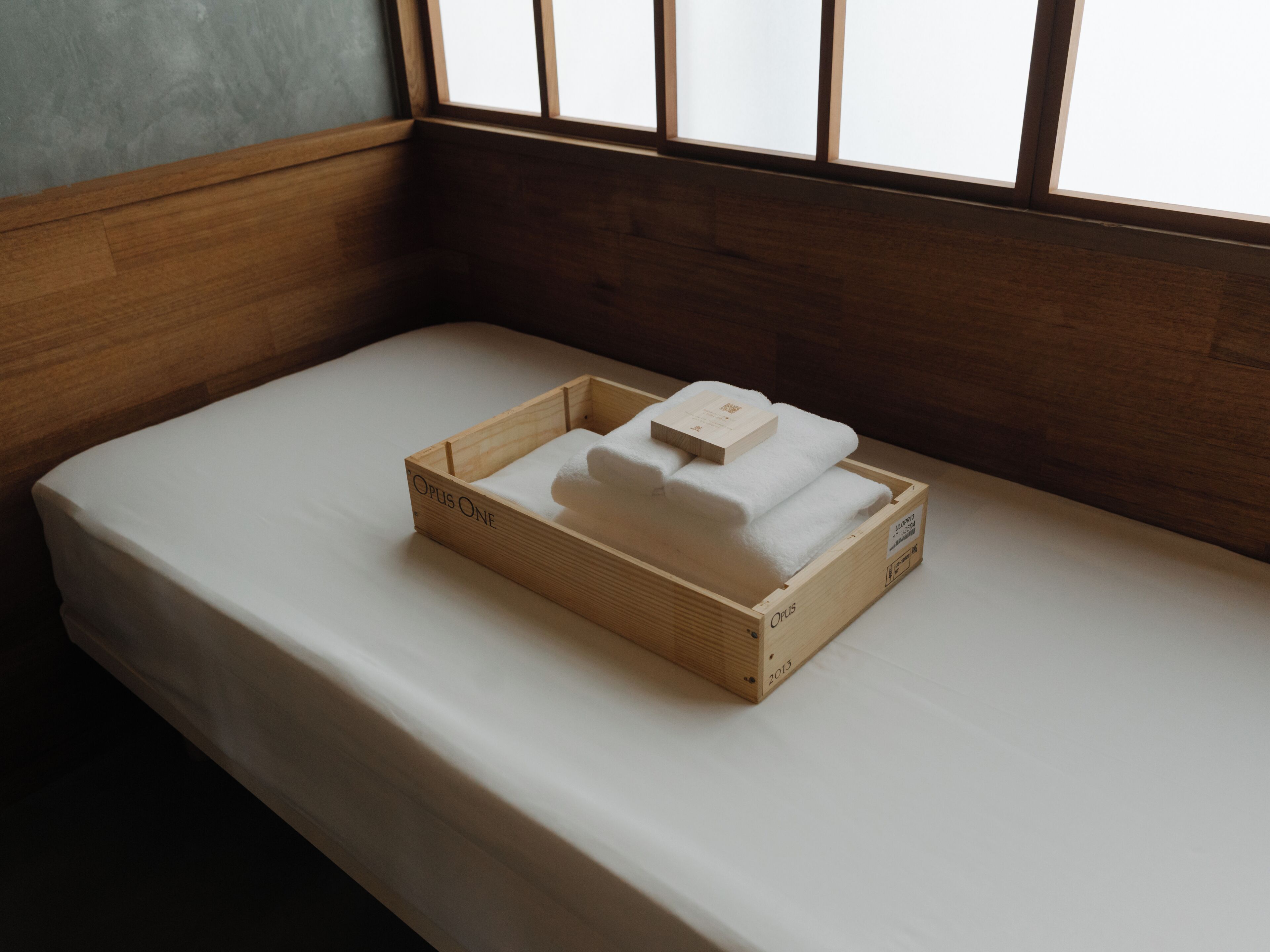 A wooden crate with a white towel and a booklet on a bed.