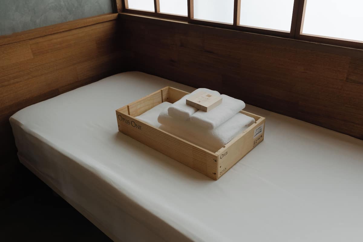 A wooden crate with a white towel and a booklet on a bed.
