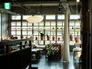 A room with a large window, wooden furniture, and potted plants. - UNTEN INN (Nago)