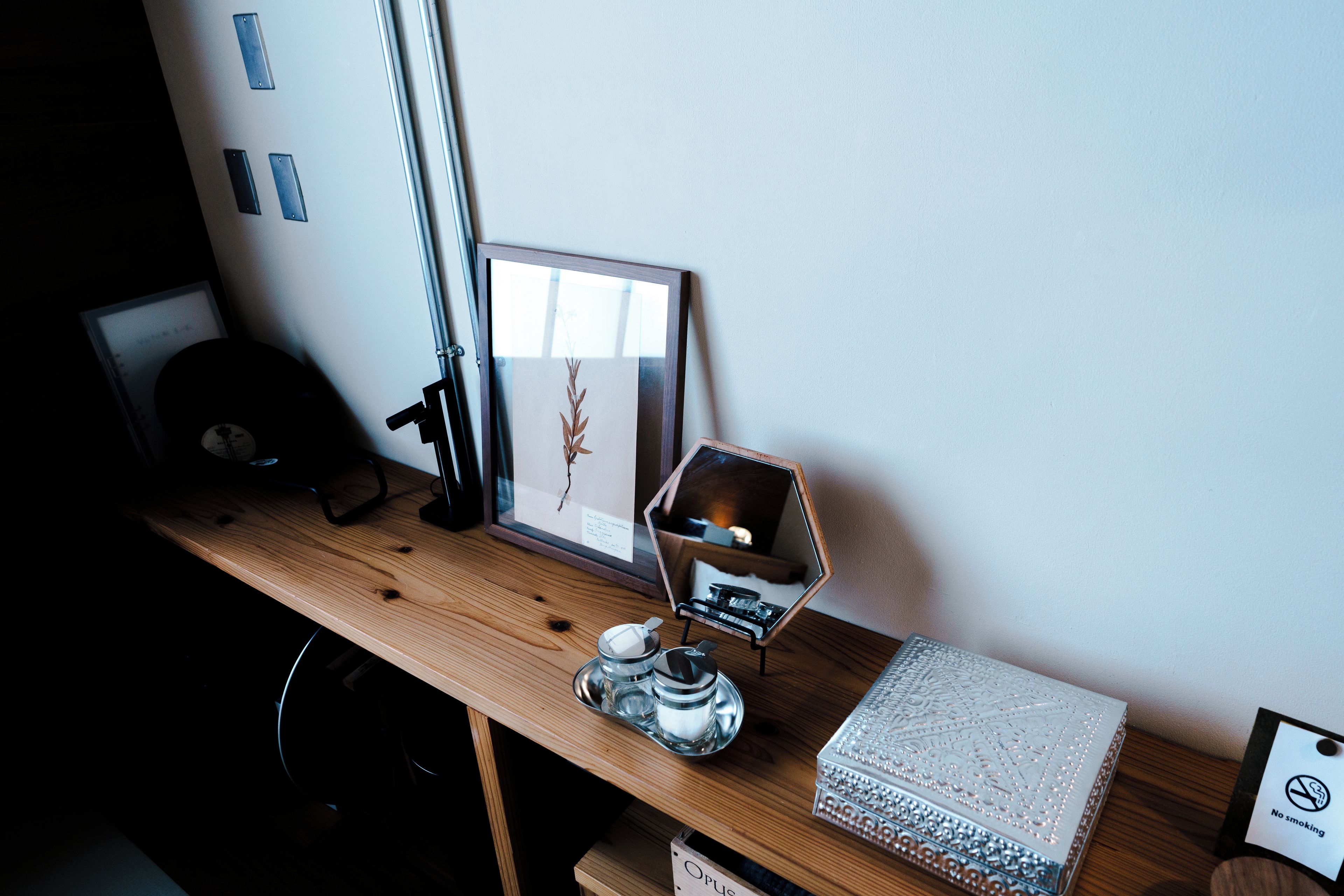 A wooden desk with a framed picture, a small mirror, a glass container, and a decorative box.