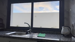 Eine Küche mit Spüle, einem Fenster und einem Wasserkocher auf der Arbeitsfläche.