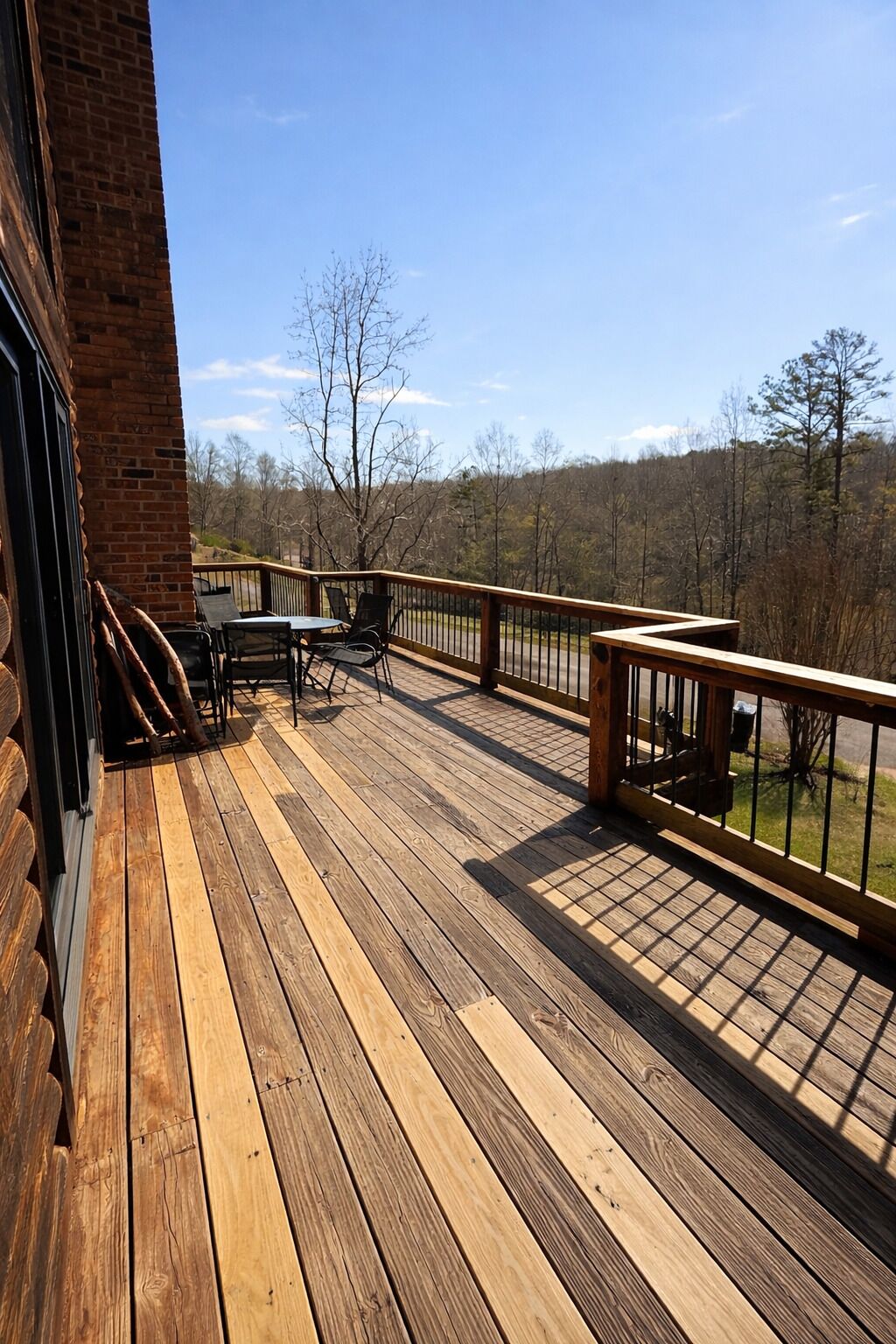 Eine Holzterrasse mit Gartenmöbeln, ein Backsteinhaus und Blick auf Bäume und Hügel.
